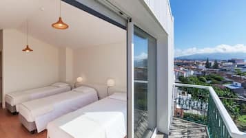 Une chambre d’hôtel moderne avec deux lits, un balcon offrant une vue sur la ville et une grande fenêtre.