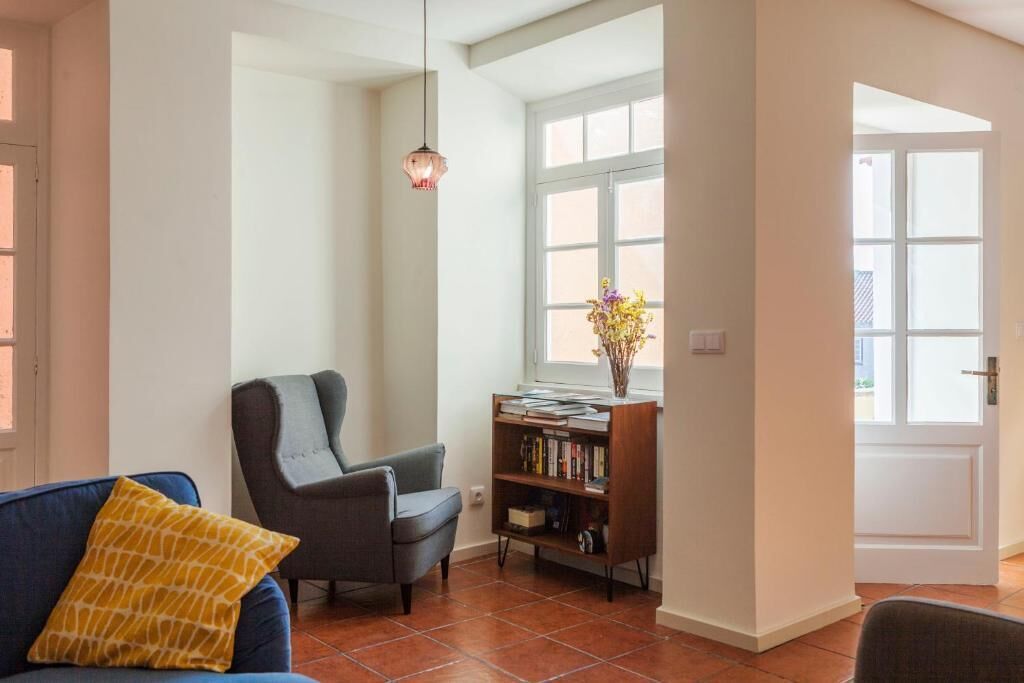 Un salon comprenant un canapé, un fauteuil, une bibliothèque et une fenêtre laissant entrer la lumière naturelle.