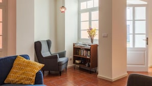 A living room with a sofa, armchair, bookshelf, and a window with natural light. - A Bica Hostel (Ponta Delgada)