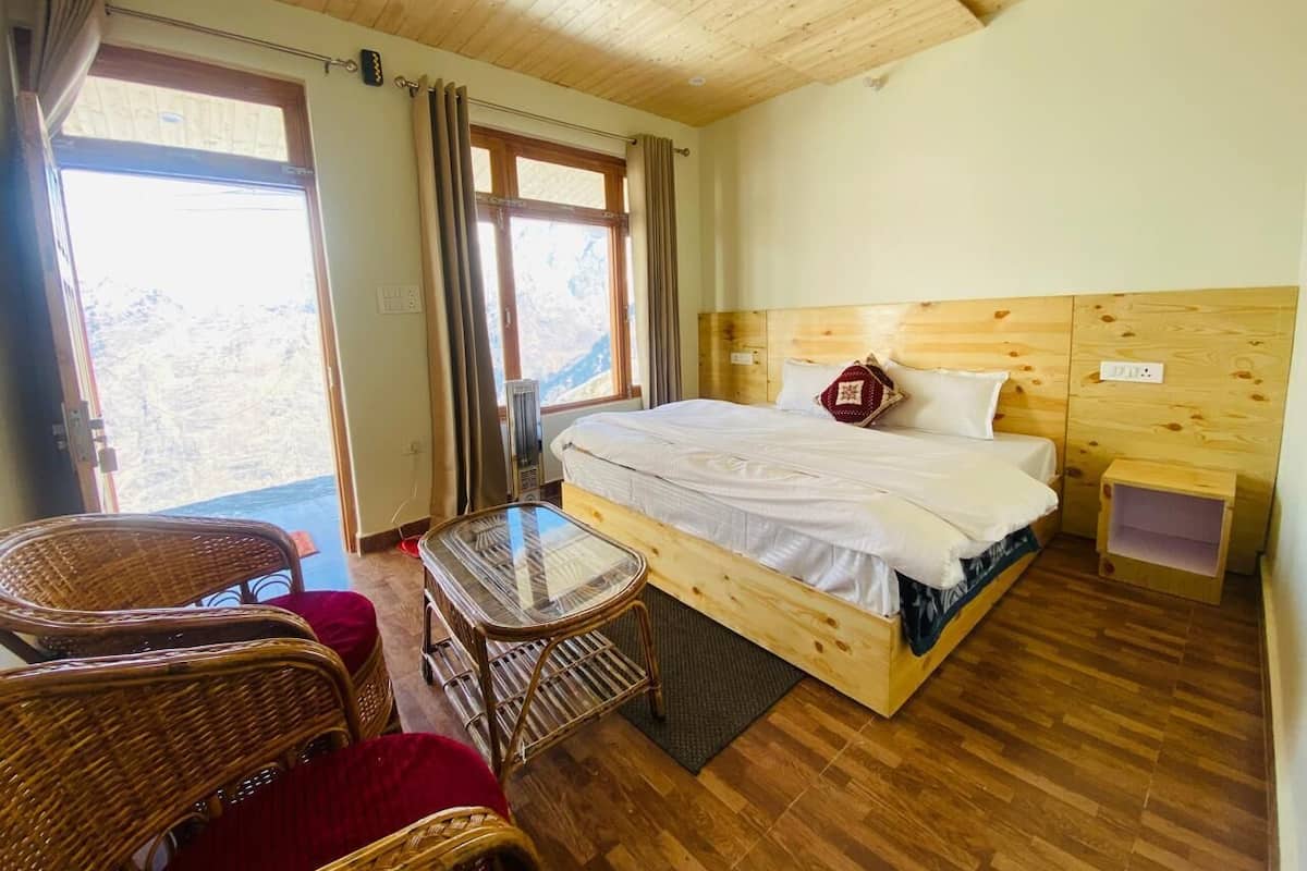 A wooden-paneled room with a bed, a small table, wicker chairs, and a view through a window.