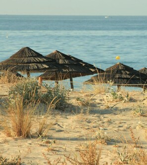 Een strand met rieten parasols en uitzicht op de zee.