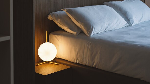 Un dormitorio moderno con cabecera de madera, una lámpara de noche y una cama bien hecha.