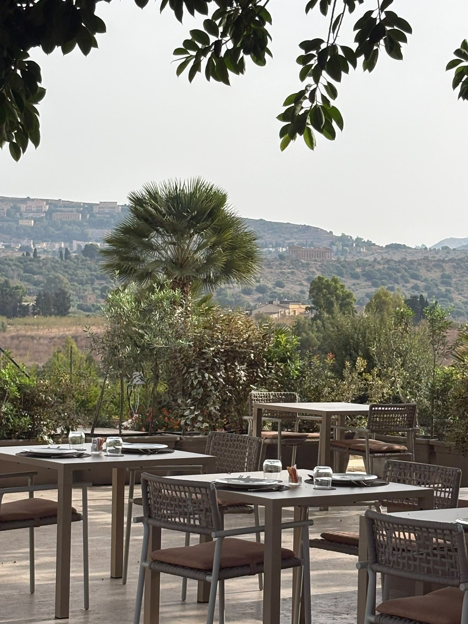 Un área de comedor al aire libre con mesas y sillas, con vistas a un paisaje montañoso.