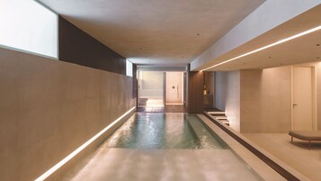 A modern interior with a long, narrow pool, a staircase, and a door leading to another room.