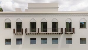 Un edificio con fachada simétrica, varios ventanales de arco y un balcón con barandilla.