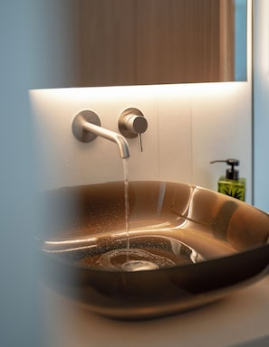 Un baño moderno con un lavabo de vidrio, un grifo y un dispensador de jabón.