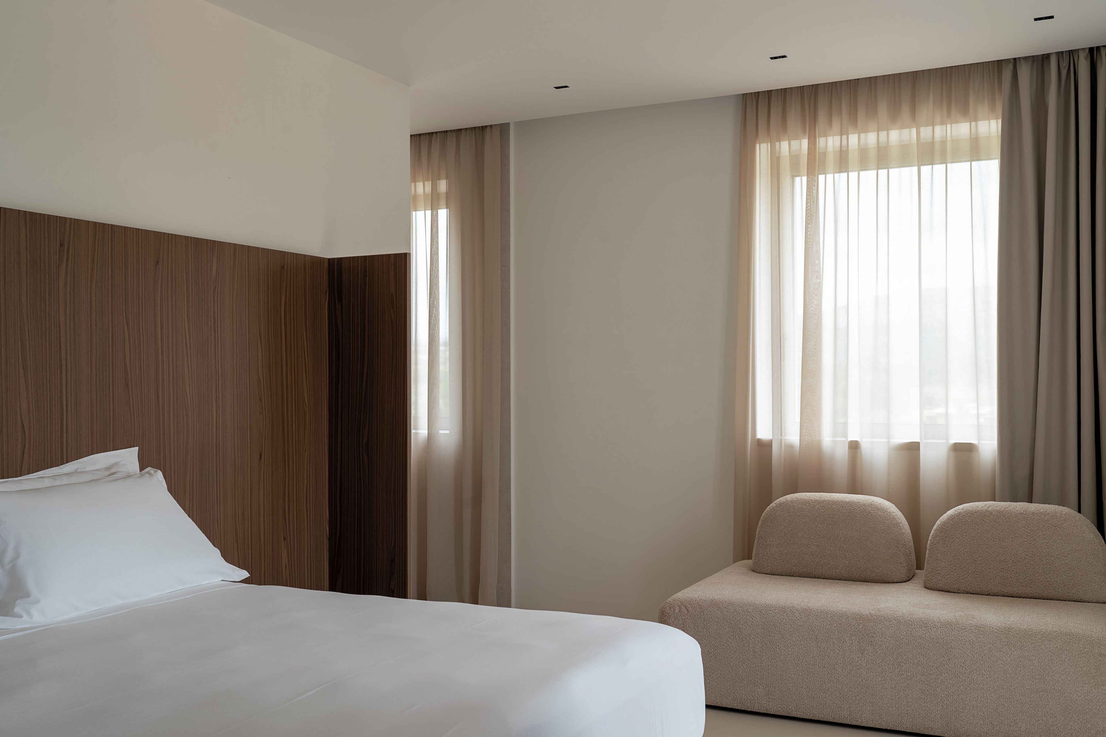 Una habitación de hotel con una cama, un sofá y un ventanal con cortinas.