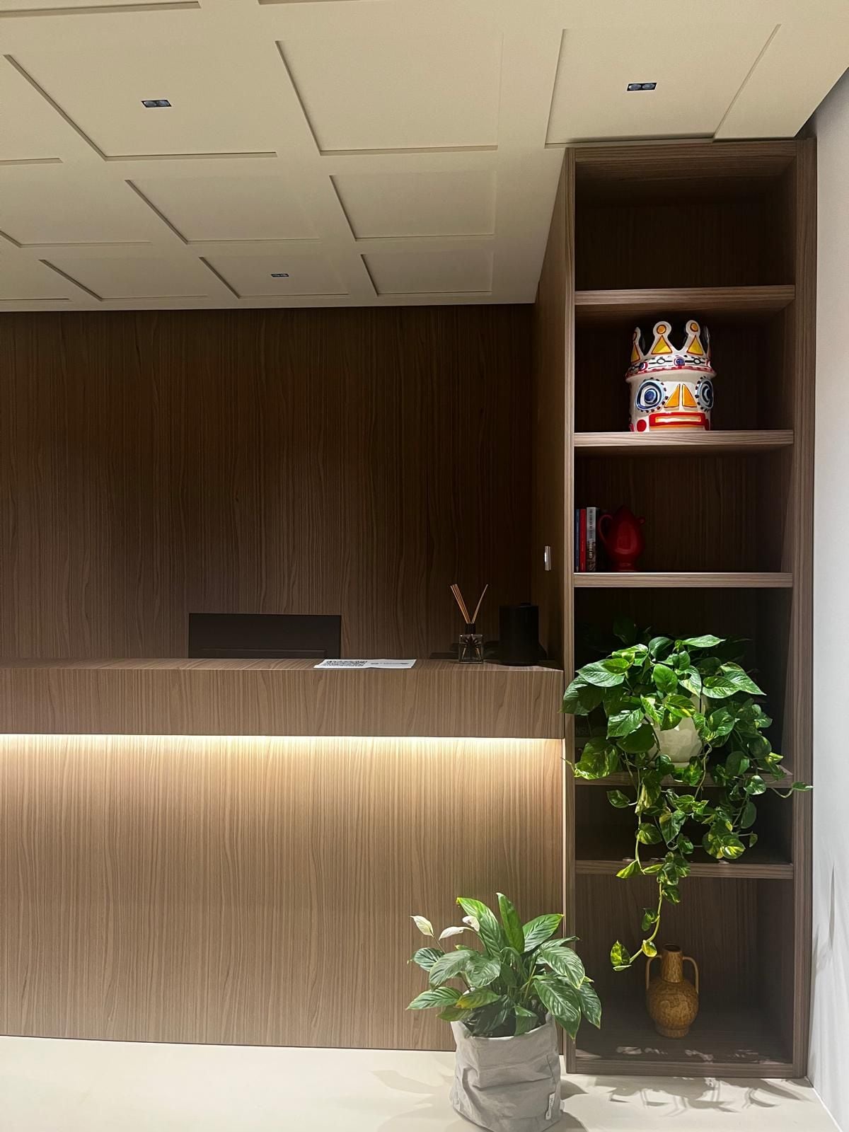 Un comptoir d’accueil avec un revêtement en bois, une plante en pot et une étagère ornée d’objets décoratifs.