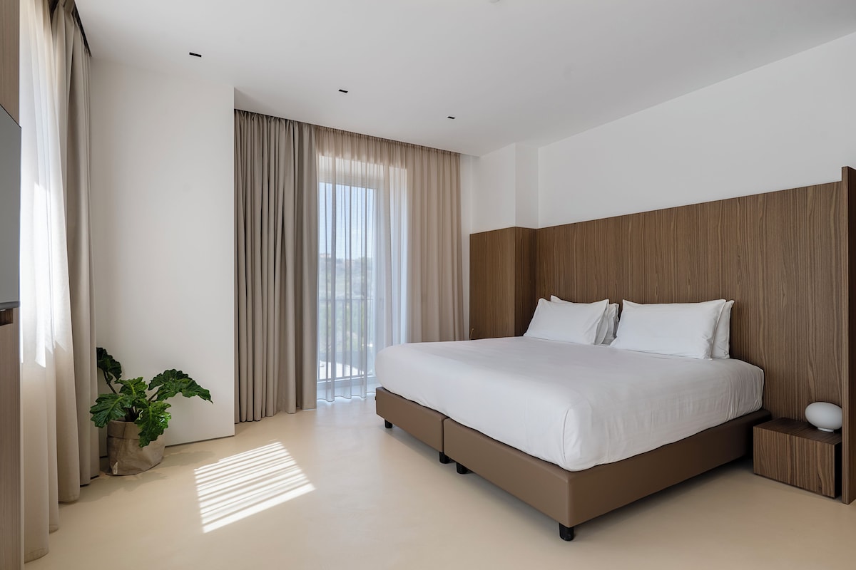 A modern bedroom with a large bed, wooden headboard, and a potted plant.