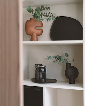 Una estantería con cafetera, un florero con hojas verdes y una escultura original.
