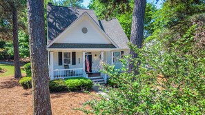 A small white house with a porch, surrounded by trees and a well-maintained lawn. - New Rental - Reynolds Lake Ocone 3 BR 2.5 Bath Cottage (Greensboro)