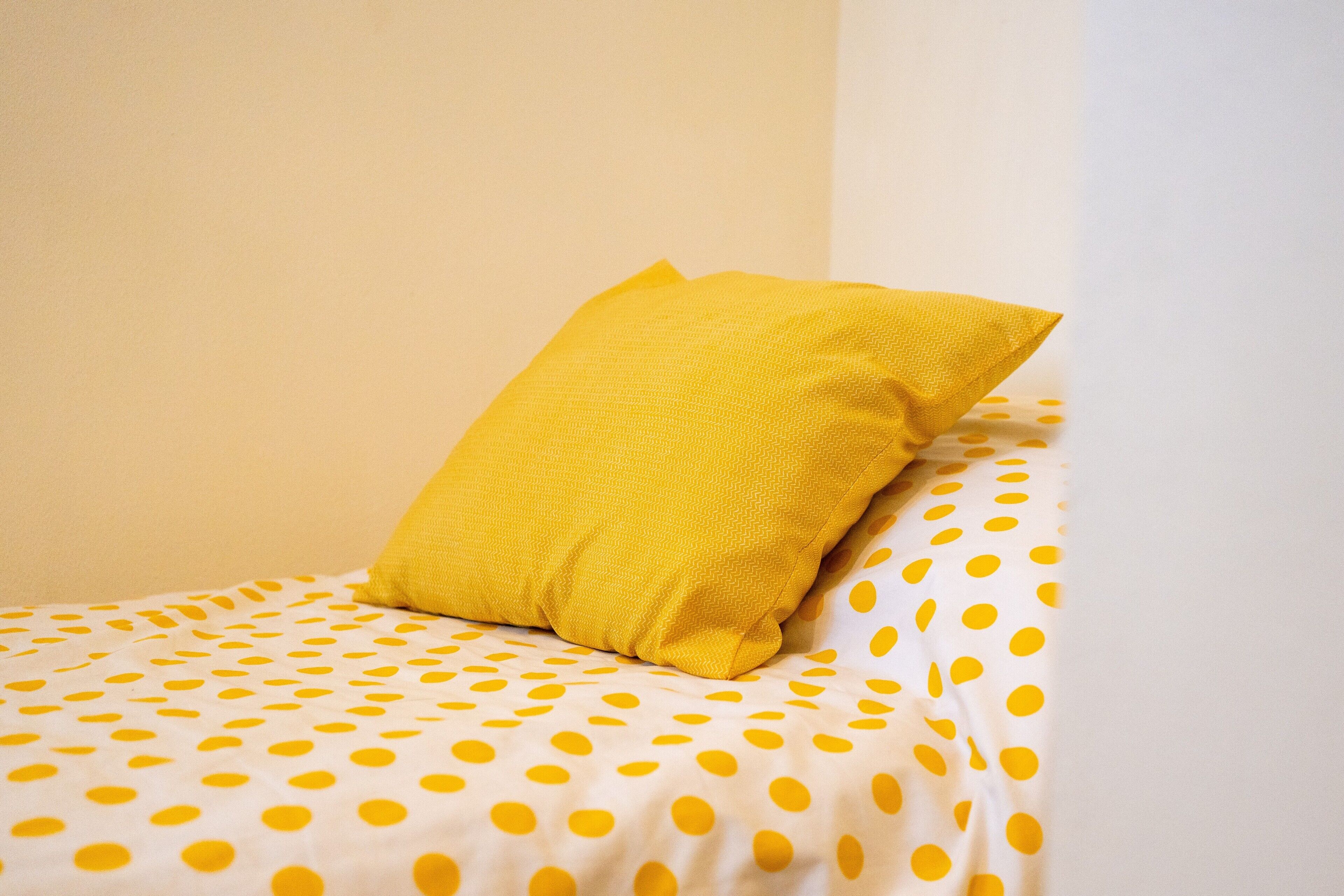 Ein Bett mit einem gelben Kopfkissen und einer weißen Bettdecke mit gelben Punkten.