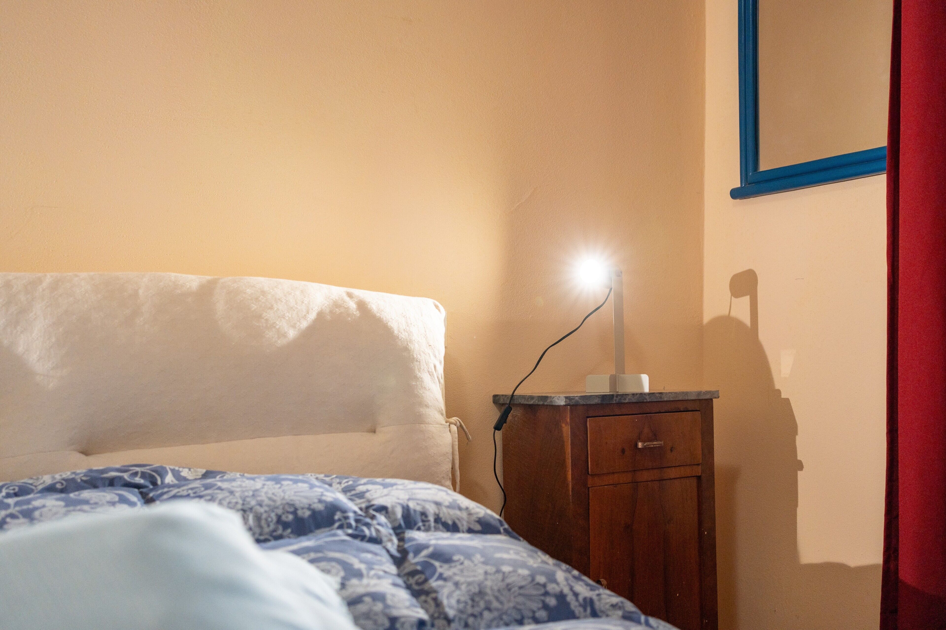 Ein Schlafzimmer mit einem Bett, einem Nachttisch, einer Lampe und einem Wandspiegel.