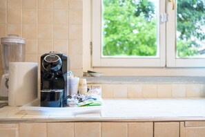 A kitchen counter with a coffee maker, a paper towel holder, and a window with a view of greenery. - Holiday Home 'La Casina All'angolo' (Civitella in Val di Chiana)