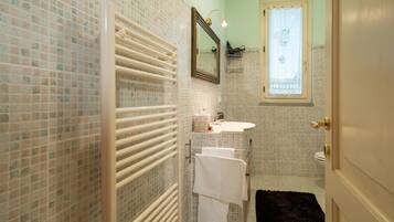 A bathroom with mosaic tile walls, a white radiator, a sink with a mirror above it, and a window with a curtain.