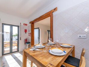 A dining area with a wooden table set for four, a mirror above, and a fire extinguisher on the wall. - Villa Sheike V3 com piscina privada (Conceição de Tavira)