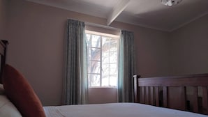 A bedroom with a bed, a window with curtains, a wooden headboard, and a ceiling light fixture. - Off-grid Cottage Mountain Views Horses & Sunset (Bergrivier)