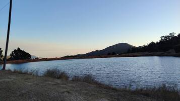 Un lago tranquilo con una montaña al fondo, rodeado de vegetación escasa y un poste de electricidad.