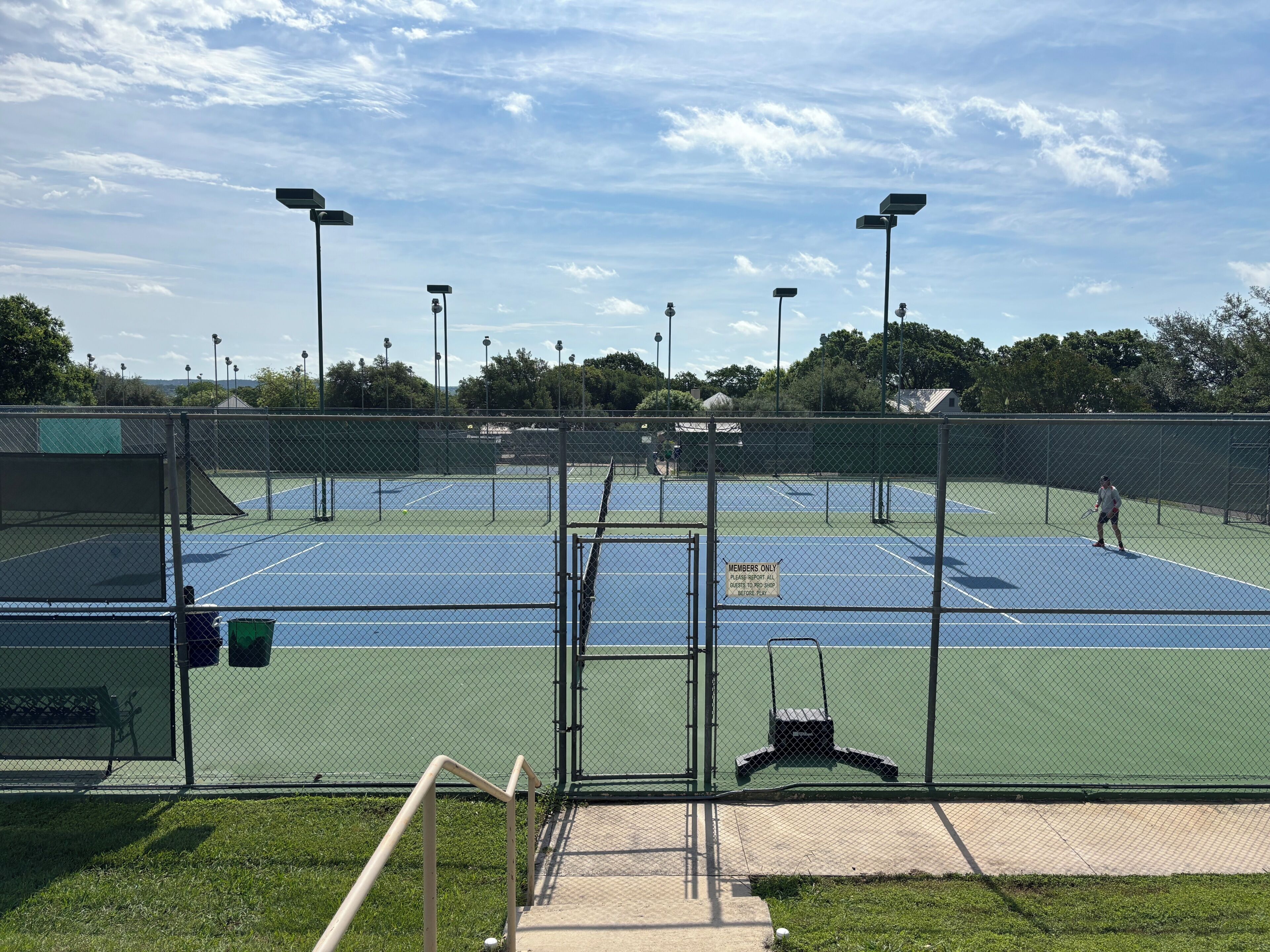 Un court de tennis entouré d’une clôture, avec un banc et un panneau indiquant qu’il est réservé aux membres.