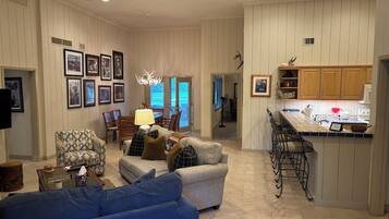 A spacious living room with a blue sofa, a dining area with a chandelier, and a kitchen with wooden cabinets.