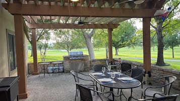 An outdoor patio with a grill, seating, and a view of a golf course.