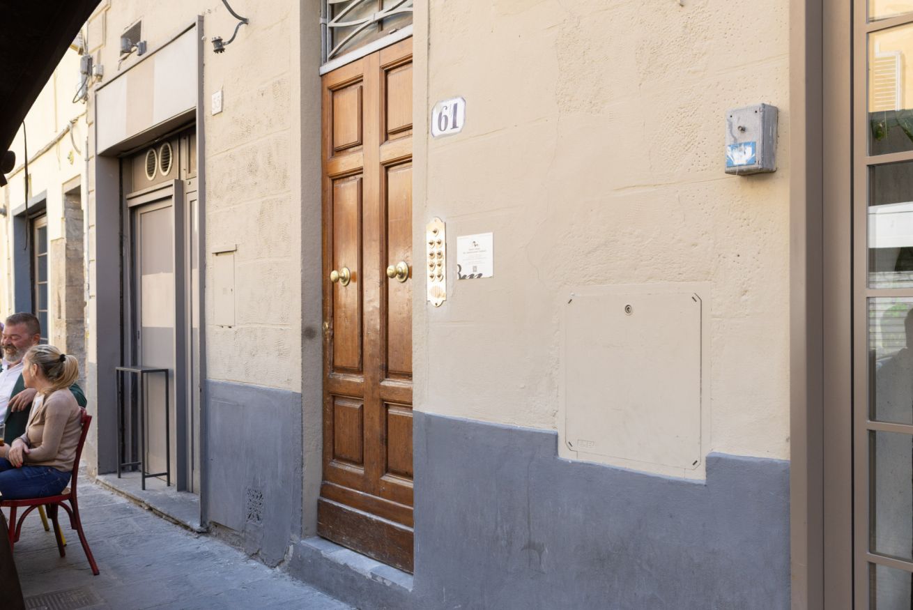 A building with a large wooden door, a number '61' sign, and a small electrical box on the wall.