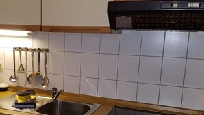 A kitchen with a stainless steel sink, a black range hood, and a hanging utensil rack.