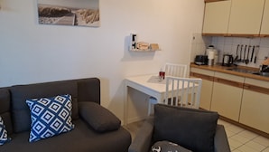 A compact living space with a sofa, armchair, small dining table, and kitchenette.