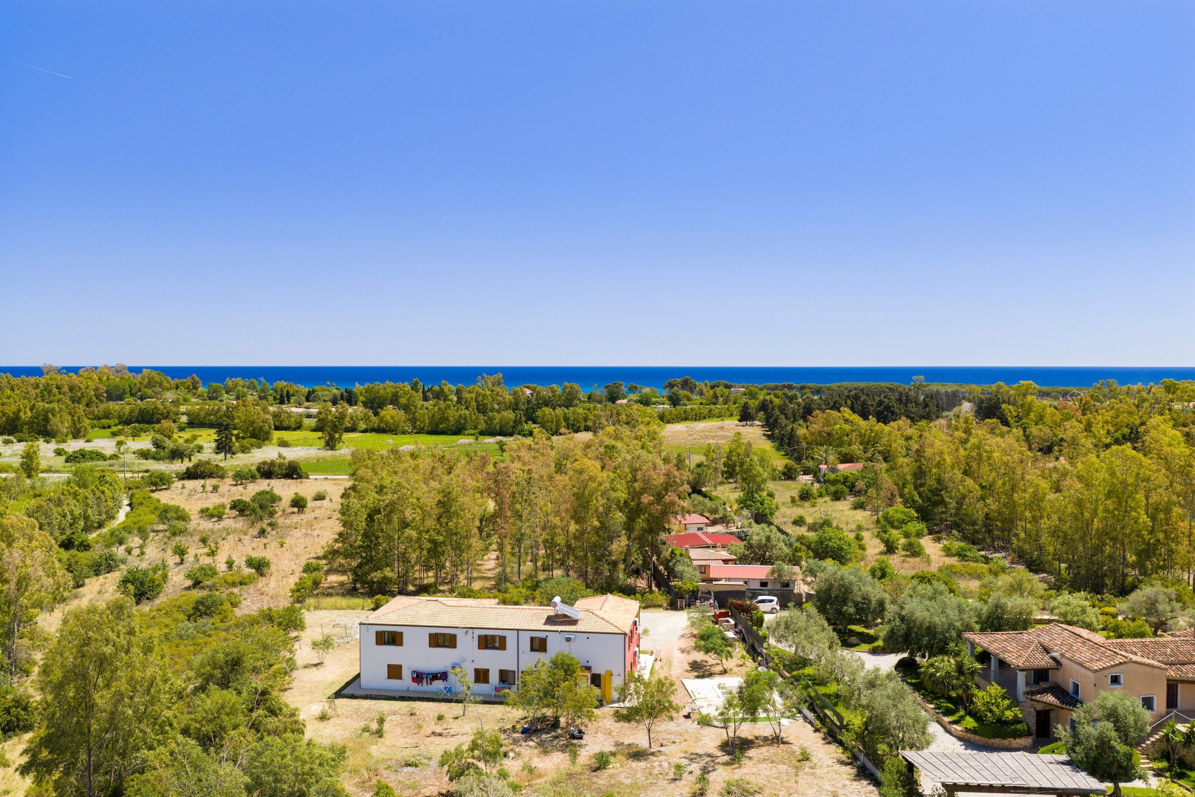 A white building with a red roof, surrounded by trees and a clear blue sky.