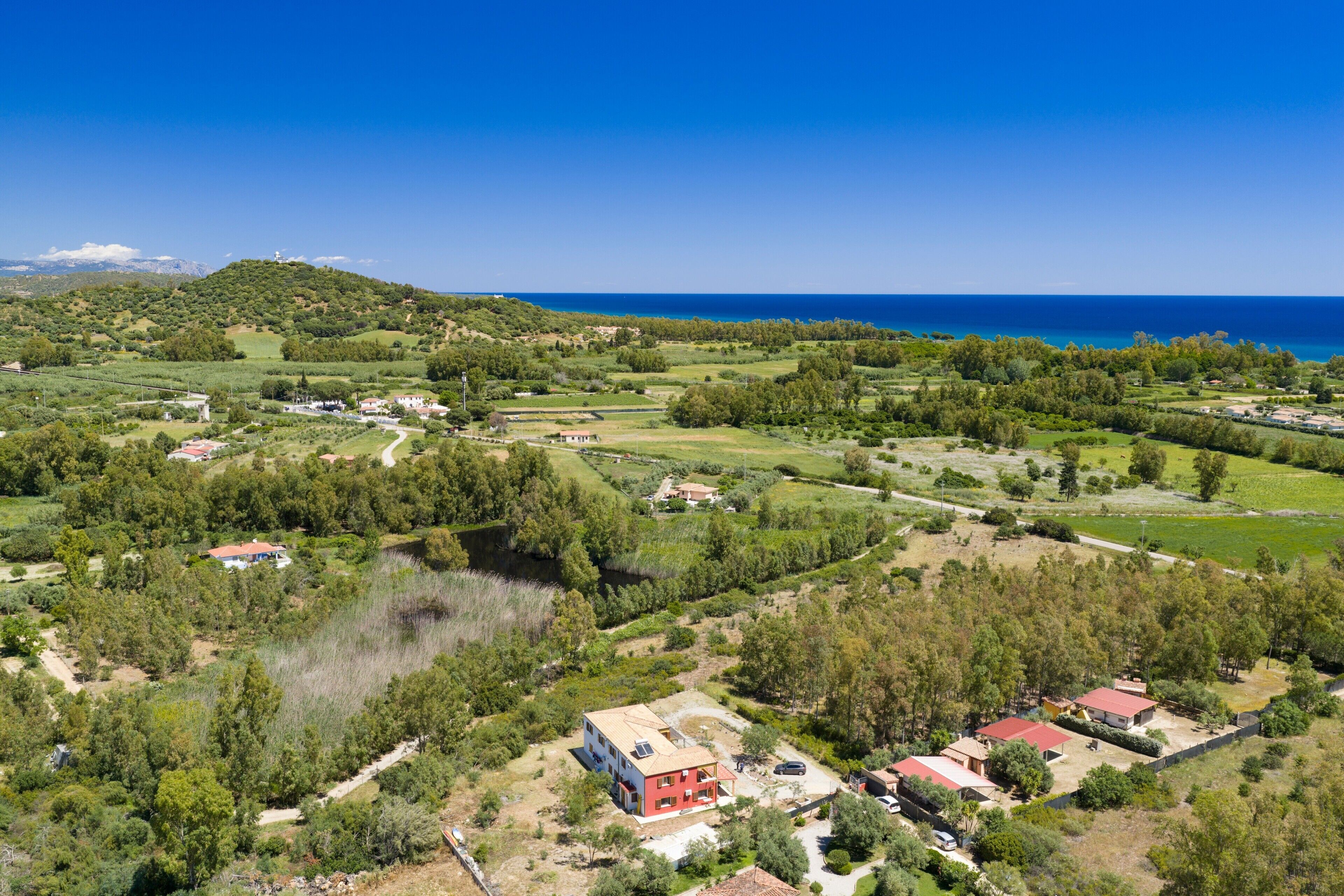 An aerial view of a coastal area with houses, greenery, and a clear blue sky.