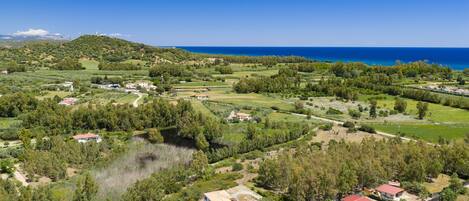 An aerial view of a coastal area with houses, greenery, and a clear blue sky.