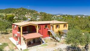 A two-story house with a red and yellow facade, a covered patio, and a view of the surrounding landscape. - Apartment 'Casa Delle Mimose Con Terrazza' with Private Terrace, Wi-Fi and Air Conditioning (Cardedu)