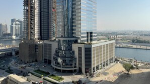 A high-rise building with a modern glass facade, surrounded by a busy urban environment with a river and other buildings. - Modern 2BR Apartment in Merano Tower (Dubai)