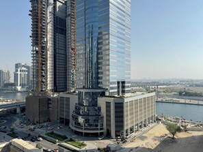 A high-rise building with a modern glass facade, surrounded by a busy urban environment with a river and other buildings. - Modern 2BR Apartment in Merano Tower (Dubai)