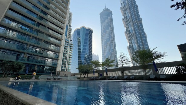 A swimming pool with lounge chairs, surrounded by high-rise buildings. - Modern 2BR Apartment in Merano Tower (Dubai)