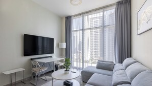 A modern living room with a flat-screen TV, a sofa, a coffee table, and a dining area with a chair and table. - Modern 2BR Apartment in Merano Tower (Dubai)