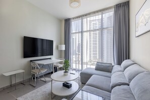 A modern living room with a flat-screen TV, a sofa, a coffee table, and a dining area with a chair and table. - Modern 2BR Apartment in Merano Tower (Dubai)