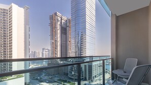 A balcony with a view of high-rise buildings, a glass railing, and a table with a chair. - Modern 2BR Apartment in Merano Tower (Dubai)
