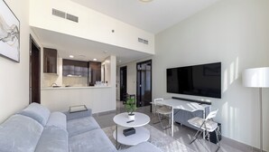 A modern living room with a sectional sofa, a round coffee table, a dining area with a TV, and a kitchen in the background. - Modern 2BR Apartment in Merano Tower (Dubai)