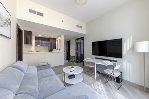 A modern living room with a sectional sofa, a round coffee table, a dining area with a TV, and a kitchen in the background. - Modern 2BR Apartment in Merano Tower (Dubai)