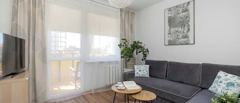 A modern living room with a sofa, a television, a round coffee table, and a large window with curtains.