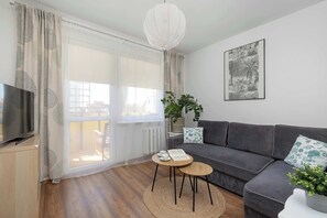 Ein modernes Wohnzimmer mit einer Couch, einem Fernseher, einem runden Couchtisch und einem großen Fenster mit Vorhängen.