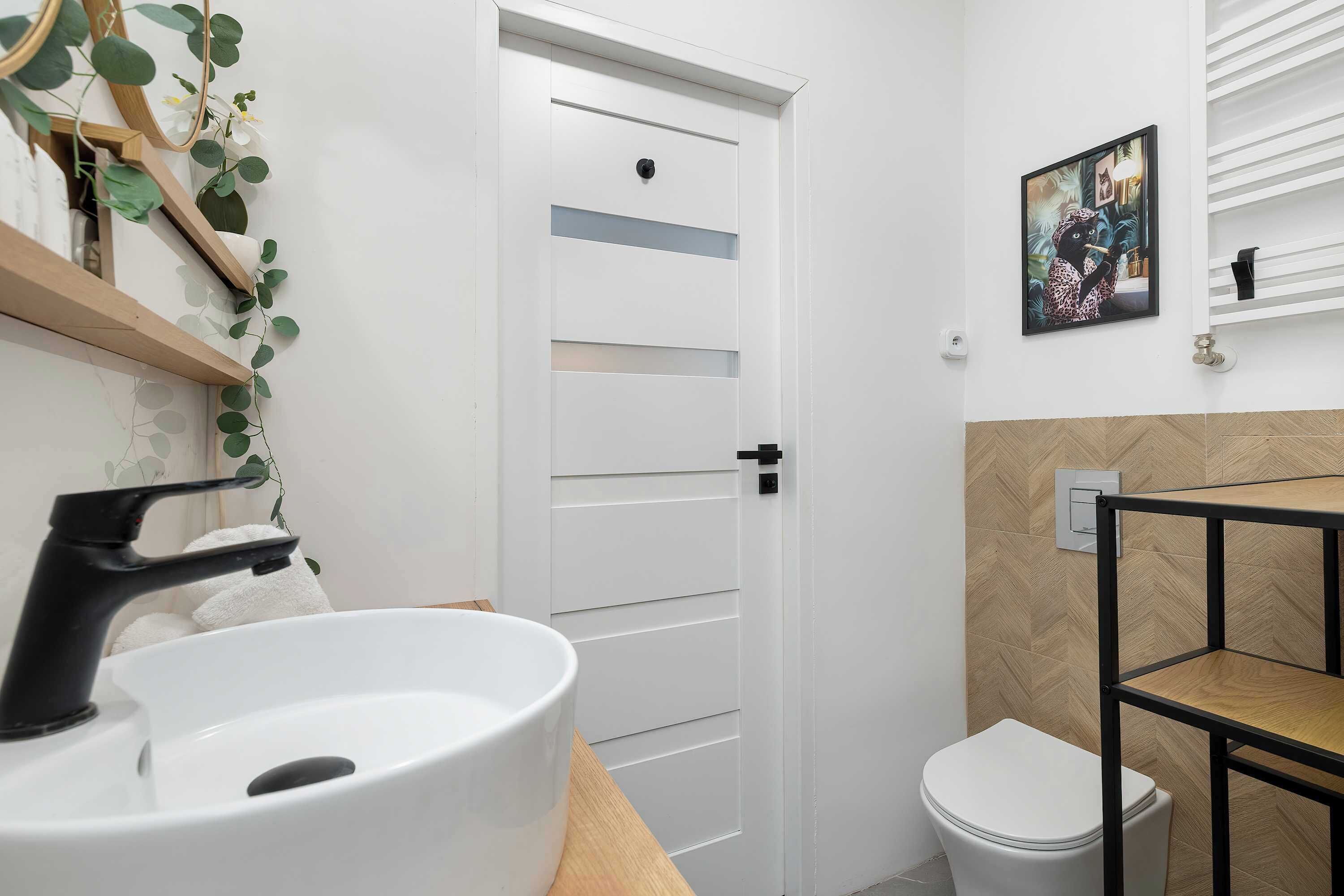 Et badeværelse med en hvid vask, toilet, en hvid dør og en hylde med et billede.