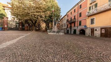 Una piazza lastricata con una statua, edifici con balconi e una bandiera.