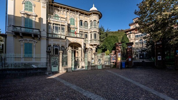 Un bâtiment historique à l’architecture riche et travaillée, doté d’une cour pavée et d’un drapeau.