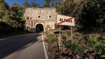 A road leading to a stone building with an archway, surrounded by greenery.