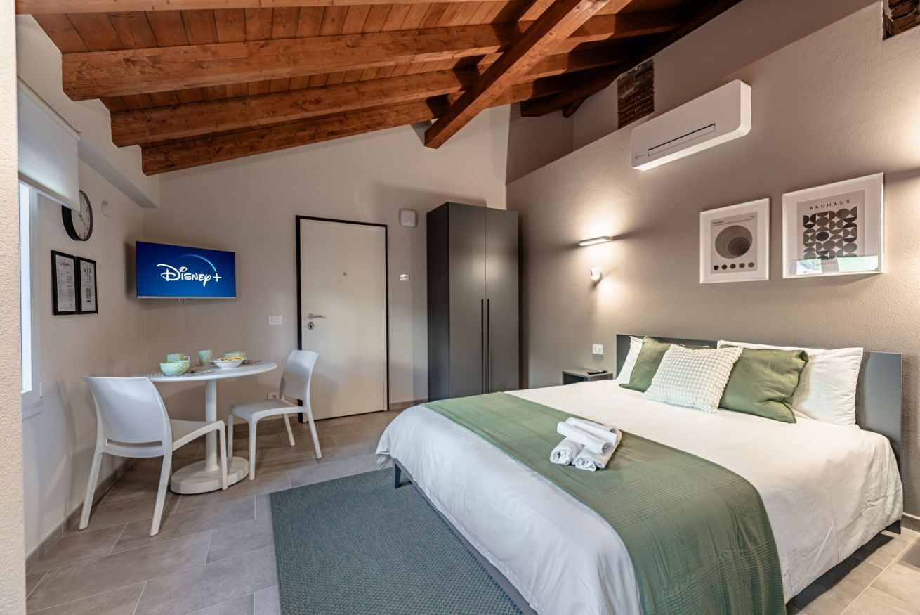 Una camera d'albergo moderna con soffitto in legno, un letto con biancheria verde, una scrivania con sedie, una televisione e un frigorifero.