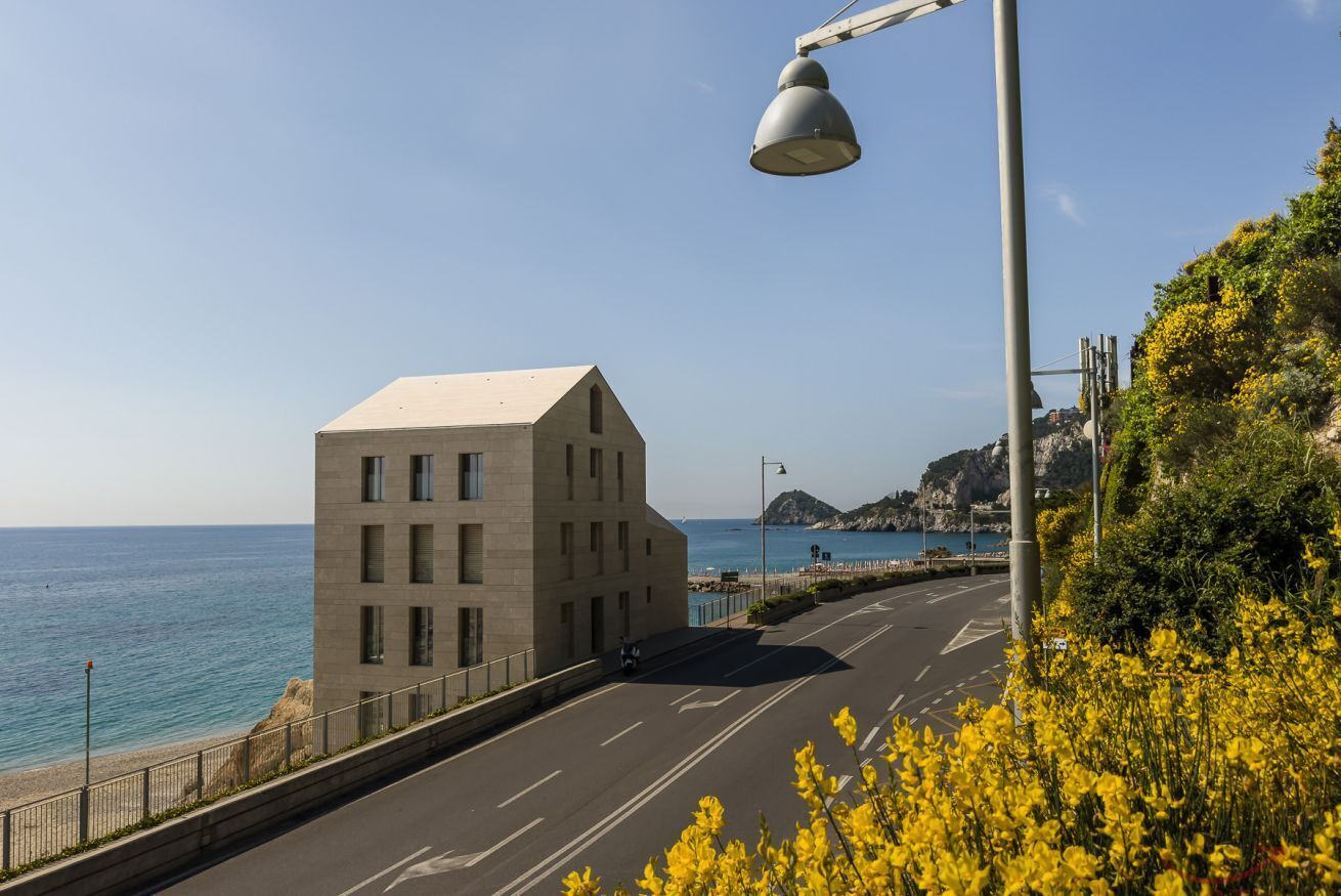 Una carretera costera con un edificio moderno, cielo despejado y vista al mar.