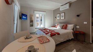 Ein Hotelzimmer mit Bett, Fernseher, Esstisch mit Tasse und Untertasse sowie einem Fenster.