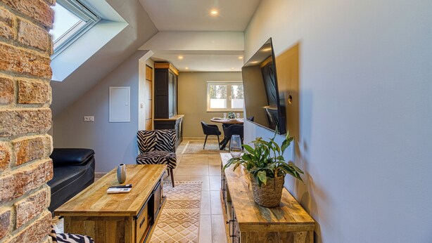 A loft-style living space with a high ceiling, skylight, a dining area with a table and chairs, a sofa, and a television mounted on the wall. - 2-bedroom apartment "Le Chaleureux (Dunkerque)